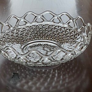 May include: A clear, oval-shaped glass serving dish with a diamond-patterned base and a decorative, openwork rim. The dish is designed with a central, raised section and is ideal for serving fruit or other items.