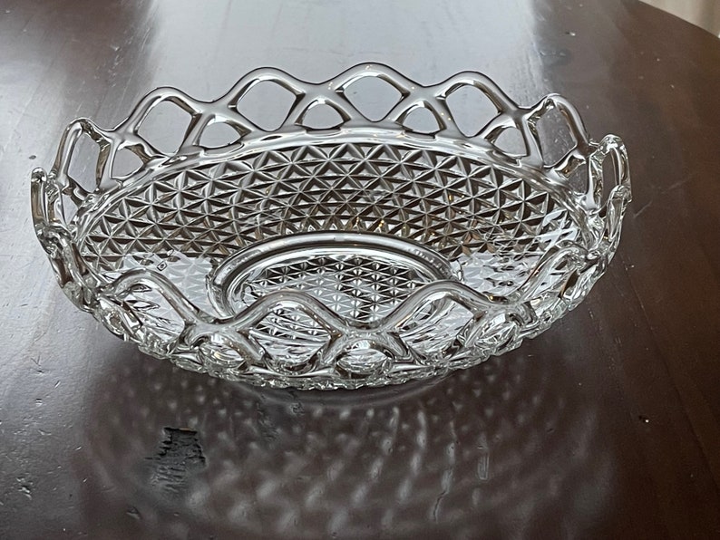 May include: A clear, oval-shaped glass serving dish with a diamond-patterned base and a decorative, openwork rim. The dish is designed with a central, raised section and is ideal for serving fruit or other items.