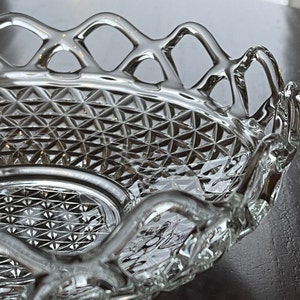 May include: A clear, oval-shaped glass serving dish with a diamond-patterned interior and a decorative, openwork rim. The dish has a scalloped edge and is designed for serving food or displaying decorative items.
