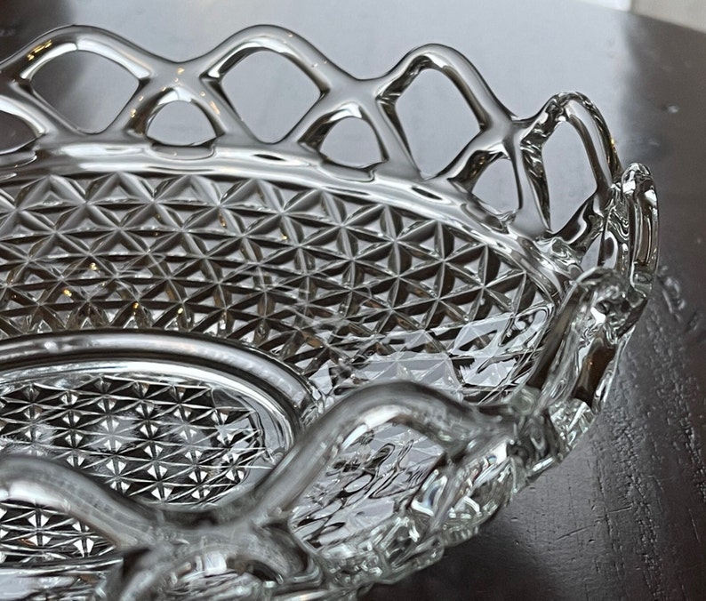 May include: A clear, oval-shaped glass serving dish with a diamond-patterned interior and a decorative, openwork rim. The dish has a scalloped edge and is designed for serving food or displaying decorative items.