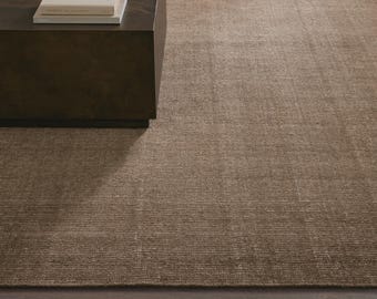 May include: A close-up of a brown rug with a textured surface. The rug is next to a dark brown, rectangular coffee table. Several books are stacked on top of the table.