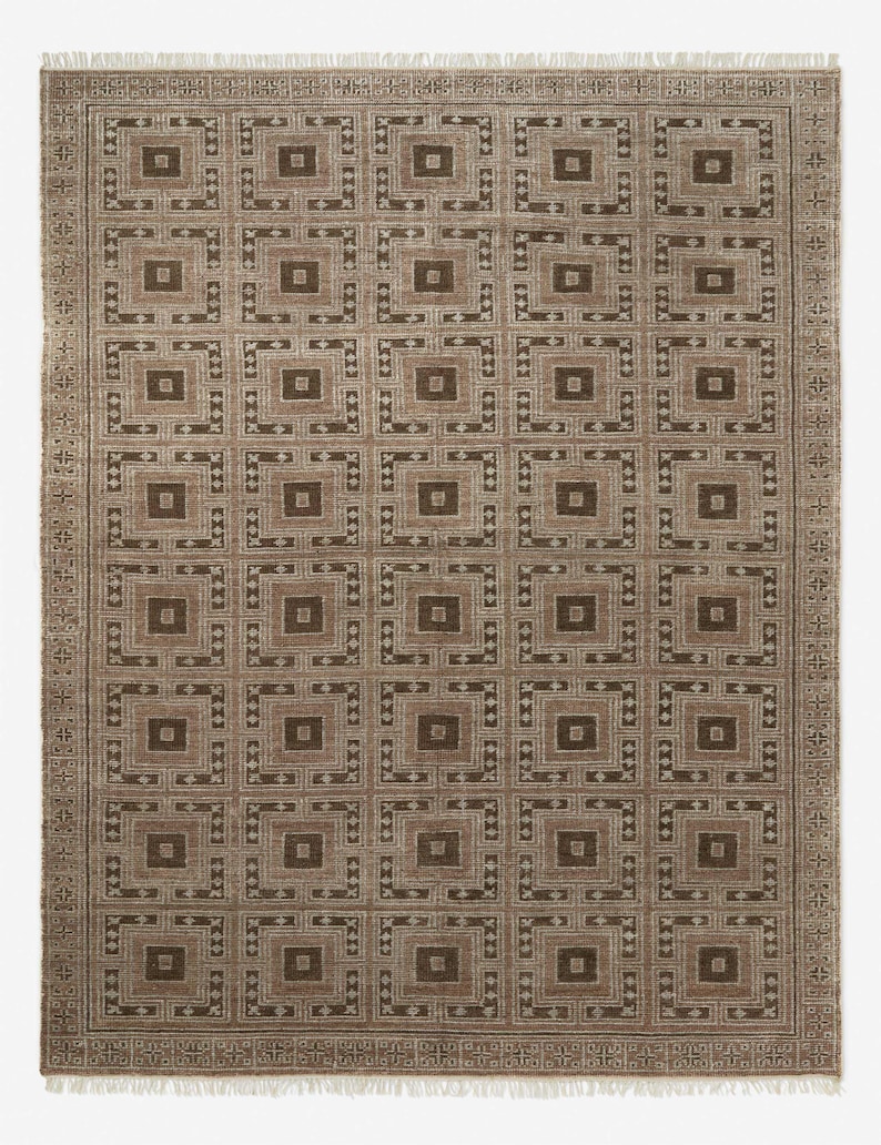 May include: A rectangular brown rug with a repeating geometric pattern of squares and rectangles. The rug has a border with a repeating design and fringe on the short ends. The color palette includes shades of brown and beige.