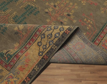May include: An olive green rug with a folded corner, revealing a patterned underside. The rug features a detailed design with teal, red, and gold accents. The border has a repeating floral pattern.