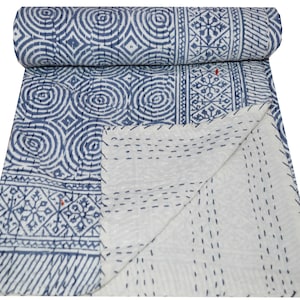 May include: A rolled-up, blue and white patterned quilt. The quilt features geometric designs, including circles and rectangular patterns. The stitching is visible, and the quilt is folded to display the white underside.