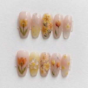 May include: A set of ten artificial nails with floral designs. The nails feature a light pink base with yellow and orange flowers, silver accents, and a clear top coat. The flowers include tulips and other detailed blossoms.
