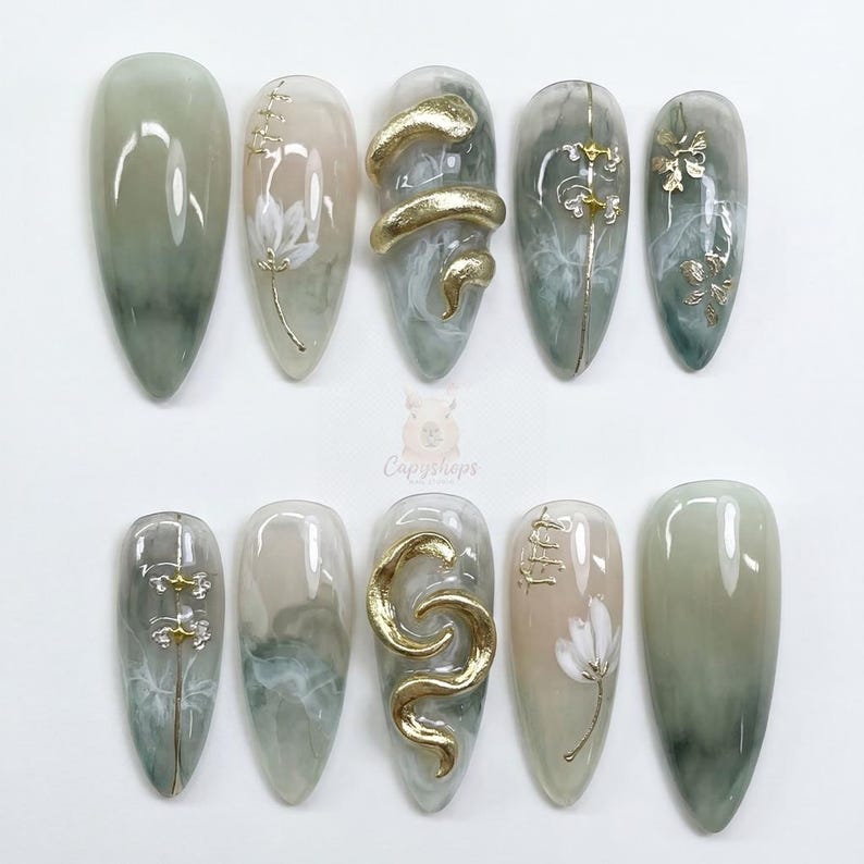 May include: A set of ten almond-shaped artificial nails. The nails feature a variety of designs, including gold snake and floral accents, and a marbled green and beige color scheme. The nails are arranged on a white surface.
