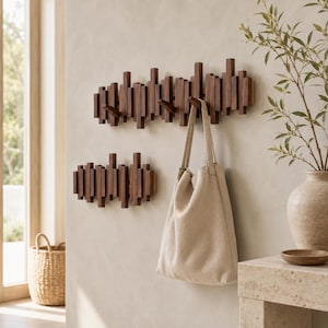 May include: Two dark brown wooden wall-mounted coat racks with a vertical slat design. The larger rack features multiple hooks, one of which holds a beige canvas tote bag. The racks are composed of rectangular wooden pieces of varying heights.