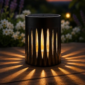 May include: A cylindrical black solar lantern featuring vertical, almond-shaped cutouts that emit a warm, golden light, casting elongated shadows on the surface below. The top of the lantern includes a solar panel, and the text digital download is visible.