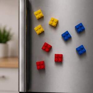 May include: A set of eight square building block magnets in primary colors of red, blue, and yellow, each featuring four circular studs on the surface. The magnets are arranged on a stainless steel refrigerator door with the text digital download.