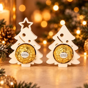May include: Two white wooden Christmas tree ornaments, each featuring a cutout star at the top and a circular opening in the center holding a gold-wrapped Ferrero Rocher chocolate. The text digital download is visible in the upper right corner.