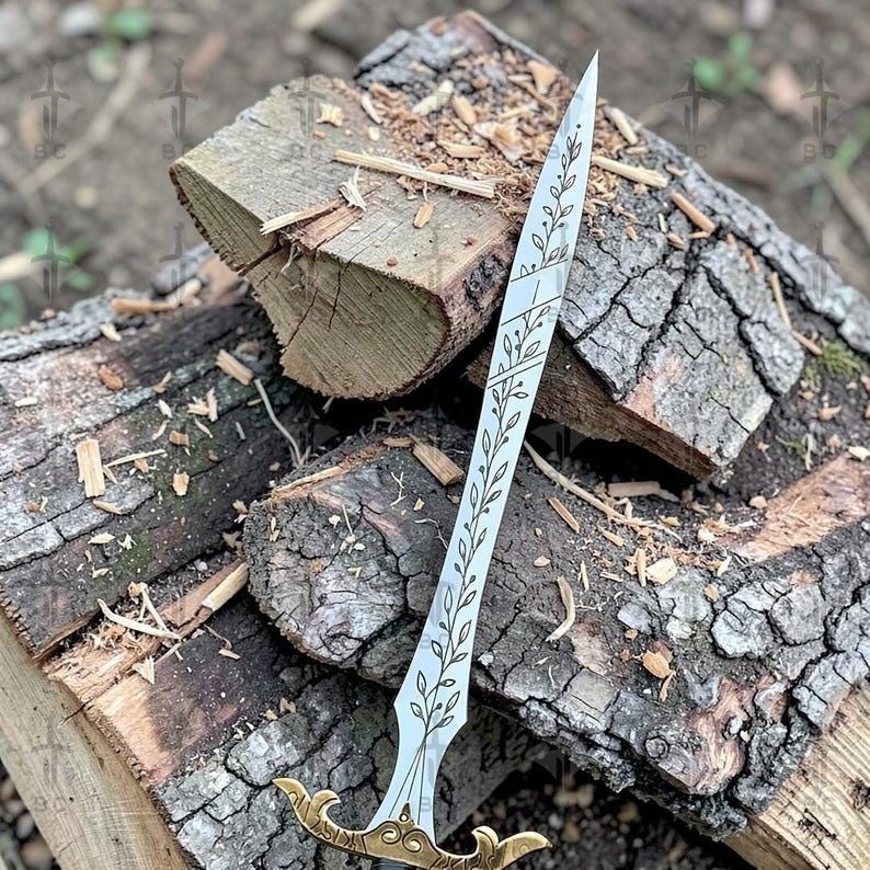 Puede incluir: Una espada plateada con empu&ntilde;adura dorada descansa sobre una pila de madera. La hoja presenta un dise&ntilde;o floral grabado. La empu&ntilde;adura tiene un dise&ntilde;o ornamentado y curvado. La espada es un objeto decorativo.