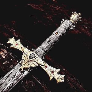 Puede incluir: Espada decorativa con empuñadura plateada y dorada y hoja estampada. La empuñadura presenta diseños intrincados y detalles rojos. La guarda de la espada es dorada con detalles ornamentados.