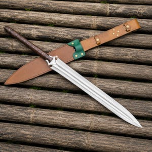 May include: A long, silver sword with a brown leather-wrapped handle and a matching leather sheath. The sword has a double-edged blade and a decorative hilt. The sheath has a green accent and a brown leather belt.
