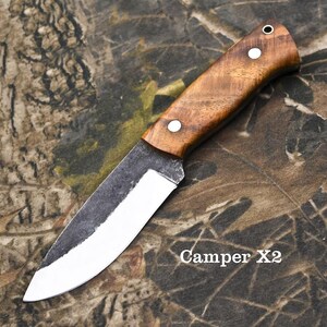Puede incluir: Un cuchillo artesanal con mango de madera y hoja plateada. El mango est&aacute; asegurado con dos remaches plateados. La hoja tiene un acabado oscuro y texturizado cerca del mango y un borde pulido. El texto "Camper X2" es visible.