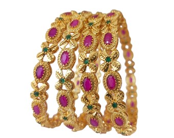 May include: A collection of gold bangles with a floral pattern. Each bangle is adorned with oval, magenta-coloured stones and small green stones. The bangles are stacked, highlighting their detailed design and craftsmanship.
