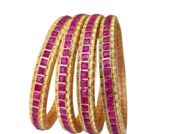 May include: Four gold bangles, each adorned with square-cut, bright pink gemstones. The bangles feature a textured, ridged pattern on the gold band. The gemstones are set closely together, forming a continuous line of colour.