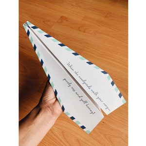 May include: A white paper airplane with blue and green stripes. The airplane has the text "When the newlyweds walk your way... gently toss and yell hooray!" printed on it.