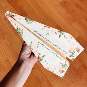 May include: A white paper airplane with a floral pattern and the text "When the newlyweds walk your way... gently toss and yell hooray!"
