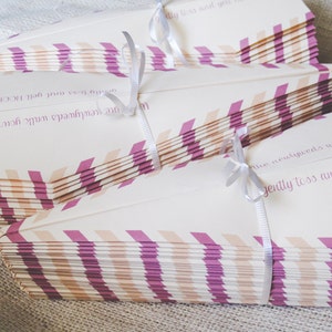 May include: Stacks of cream-colored wedding confetti packets tied with white ribbon. Each packet has a diagonal pattern of alternating pink and peach stripes. Text in a purple script reads, "...the newlyweds walk your way... gently toss and yell HOORAY!"