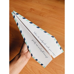 May include: A white paper airplane with blue and green stripes. The airplane has the text "When the newlyweds walk your way... gently toss and yell hooray!" printed on it.