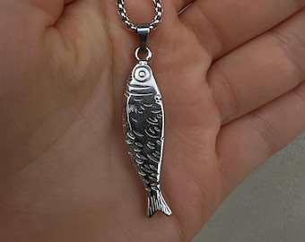 May include: A silver-coloured metal pendant shaped like a fish, featuring engraved scale and eye details. The pendant hangs from a matching silver-coloured box chain necklace, showcasing a polished, reflective surface and a simple, clean design.