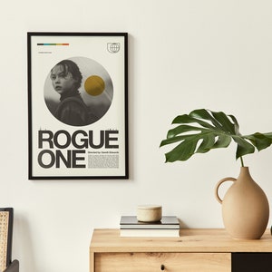 May include: A black framed poster with a minimalist design featuring a grayscale image of a young woman with a yellow circle behind her. The poster reads "Rogue One" in bold black text.