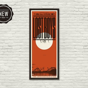 May include: A vertical rectangular poster in a black frame featuring the title LOST BOYS in bold black letters. Below the text is a large white circle against an orange background, with silhouettes of figures and a roller coaster at the bottom.