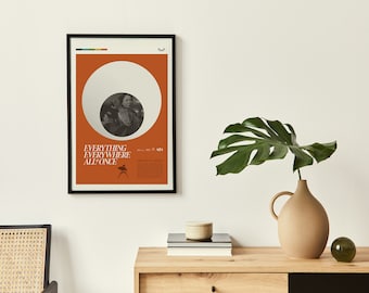 May include: A framed movie poster with an orange background and a white circle in the center. The circle contains a black and white photo of a woman. The text on the poster reads "Everything Everywhere All at Once".