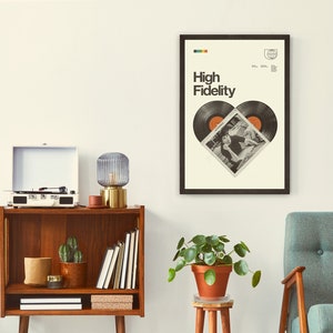 Op de afbeelding: Een ingelijst drukwerk met een witte achtergrond en zwarte tekst die "High Fidelity" luidt. De print toont een hartvorm gemaakt van twee zwarte vinylplaten met een foto van een stel in het hart.