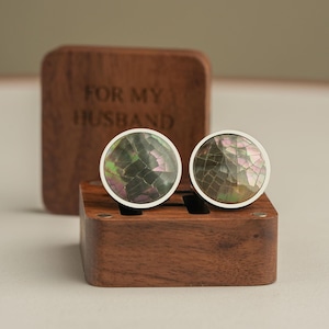 以下が含まれることがあります： イリデセントでひび割れた模様の顔とシルバーカラーの縁が付いた、丸いカフスボタンのペア。 「FOR MY HUSBAND」と刻まれた木箱に入っています。 カフスボタンは木製のホルダーに展示されています。
