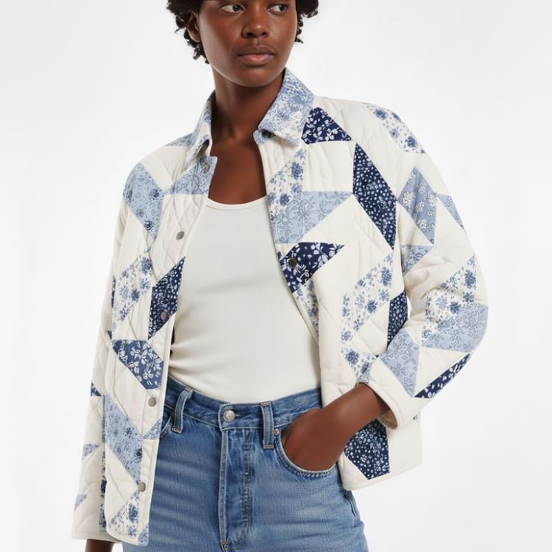 May include: A cream-coloured quilted jacket with a patchwork design. It features blue floral and geometric patterns. The jacket has a button-up front, a collar, and long sleeves. It is worn with a white top and blue jeans.