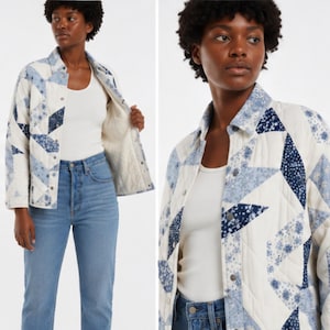May include: A quilted jacket featuring a patchwork design of cream, light blue, and dark blue floral patterns. The jacket has a classic collar, long sleeves, and a front button closure with metallic snaps. It is worn over a white tank top and blue jeans.