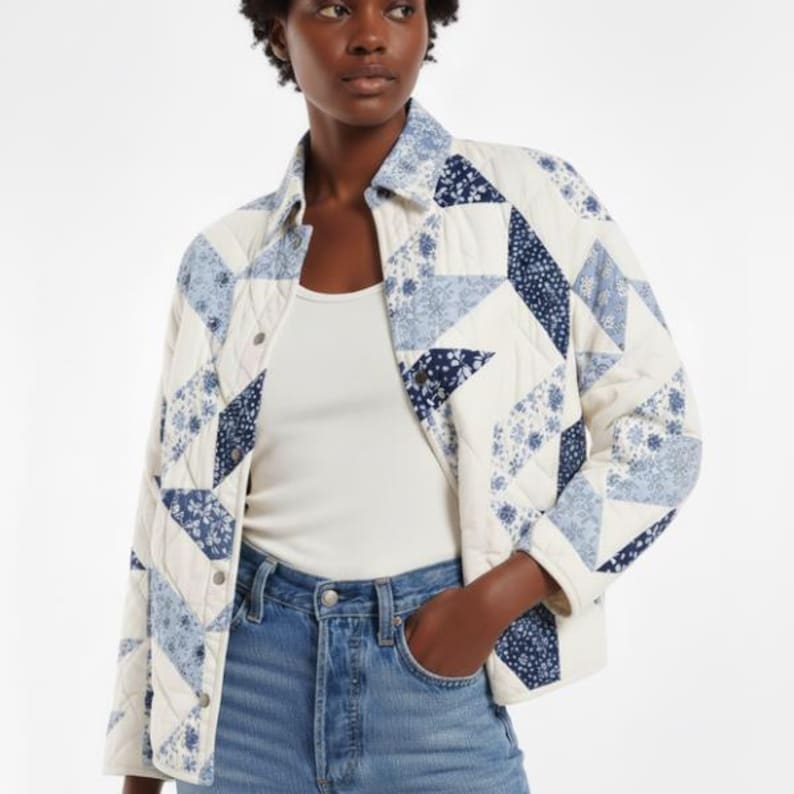May include: A quilted jacket in a patchwork design. The jacket features a cream-colored base with blue floral and geometric patterns. It has a button-down front, a collar, and long sleeves. The jacket is worn over a white top and blue jeans.