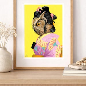 May include: A framed art print featuring an owl with a geisha hairstyle and attire. The owl's head is in profile, set against a bright yellow background. The geisha's kimono is pink with yellow floral designs. The artwork is displayed on a wooden surface.