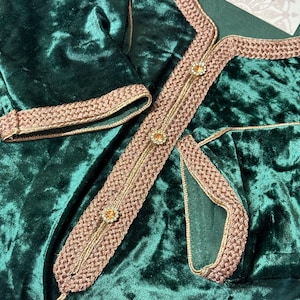 Può includere: Abito in velluto verde smeraldo con finiture dorate e marroni intricate. La finitura è dettagliata con piccoli abbellimenti scintillanti. L'abito ha un aspetto morbido e strutturato e una sensazione lussuosa. Il design include una scollatura e dettagli delle maniche decorativi.