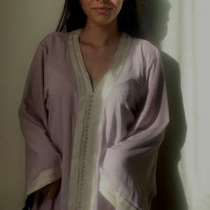 May include: A light purple robe with a V-neck and long sleeves. The robe has white trim along the edges and down the front. The model is wearing the robe.