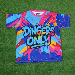 May include: A brightly coloured t-shirt with a blue base and a design of pink, orange, and yellow paint splashes. The text "DINGERS ONLY" is displayed in a bold, stylized font across the front of the shirt.