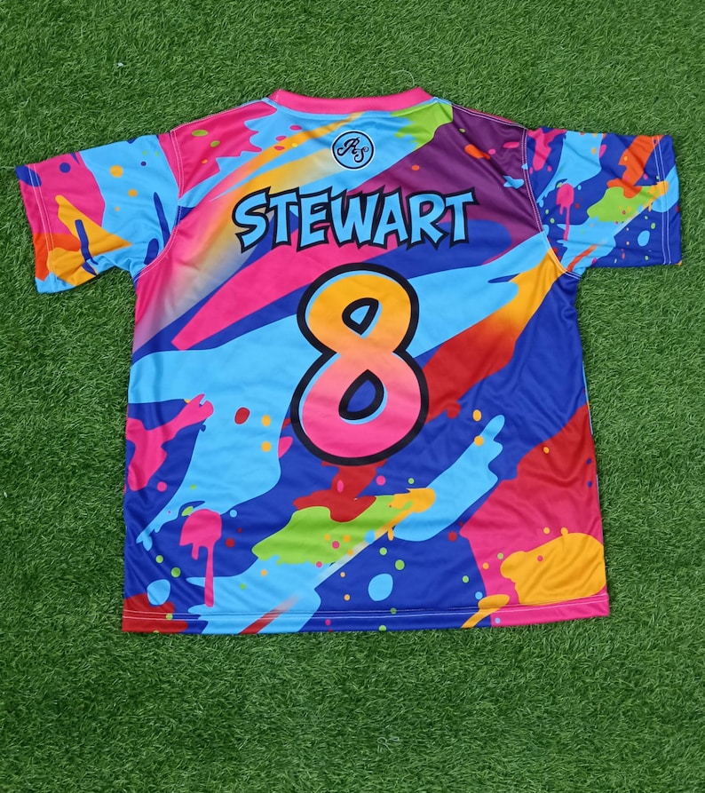 May include: A brightly coloured short-sleeved jersey with an abstract design. The jersey displays the name "STEWART" above the number "8". The colour scheme includes blue, pink, orange, and purple, with paint splatter effects.