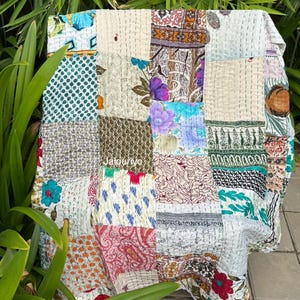 Può includere: Una trapunta patchwork con una varietà di motivi e colori di tessuto, tra cui disegni floreali, a pois e geometrici. La trapunta è composta da quadrati cuciti insieme con cuciture visibili. La parola "Jaipuriyo" è visibile sulla trapunta.