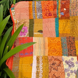 Puede incluir: Un edredón de retazos con una vibrante mezcla de colores que incluye naranja, amarillo y rosa. El edredón presenta patrones florales y geométricos, con costuras visibles. La palabra "Jaipuriyo" está impresa en el edredón.