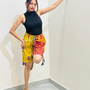May include: A black sleeveless mock neck top paired with knee-length shorts featuring a split design. The left side is mustard yellow with small blue floral patterns, while the right side is red with a yellow floral print. The text Jalpuriyo is visible.