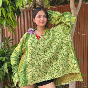 Puede incluir: Un suéter con capucha de manga larga que presenta un vibrante estampado floral verde con costuras visibles al estilo kantha. La prenda tiene un corte holgado y amplio, un dobladillo asimétrico y un pequeño detalle estampado en morado y blanco.