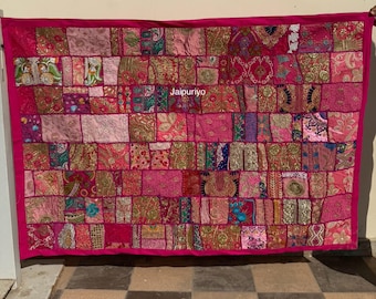 May include: A rectangular patchwork textile in shades of pink, fuchsia, and gold. The textile is composed of numerous fabric squares with various patterns and textures. The edges are framed with a solid fuchsia border. The text "Jaipuriyo" is visible on the textile.