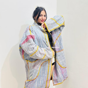 May include: A long-sleeved, open-front jacket made from quilted fabric featuring a light blue, grey, and white striped pattern with vibrant yellow trim and pink accents. The garment displays the text Jaipuriyo printed on the front panel.