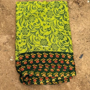 May include: A folded textile with a bright green floral design on a lime green backdrop. The lower border is dark green with a repeating pattern of orange and yellow roses. The fabric is likely a saree or similar garment.