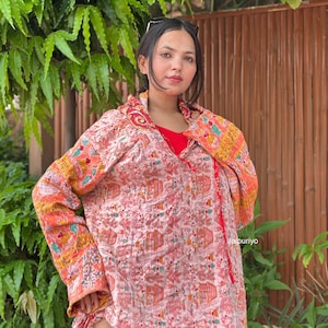 May include: A long-sleeved jacket featuring a light pink base with an intricate red and orange pattern of trees and figures. The garment has a wide collar, a wrap-style front closure with red ties, and a quilted texture throughout the fabric.