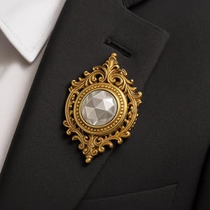 Puede incluir: Broche dorada con un dise&ntilde;o ornamental de filigrana. La broche presenta una piedra central facetada, de forma ovalada y color plateado. La broche est&aacute; prendida a una chaqueta de traje negra, con un cuello de camisa blanco visible.