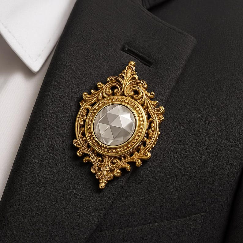 Puede incluir: Broche dorada con un dise&ntilde;o ornamental de filigrana. La broche presenta una piedra central facetada, de forma ovalada y color plateado. La broche est&aacute; prendida a una chaqueta de traje negra, con un cuello de camisa blanco visible.