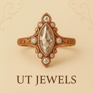 Puede incluir: Un anillo de oro rosa con una piedra central de diamante talla marquesa, rodeada de diamantes redondos más pequeños. El anillo presenta intrincados detalles de filigrana y el texto "UT JEWELS" en la parte inferior.