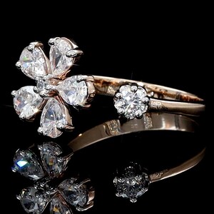 Puede incluir: Un anillo de oro rosa con un diseño floral con piedras preciosas claras en forma de pera y una piedra preciosa redonda. El anillo está sobre un fondo negro, con un reflejo debajo.